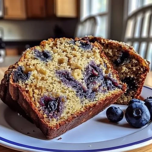Loaf of freshly baked blueberry banana bread with blueberries and banana slices on top.