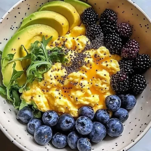 Colorful breakfast bowl with scrambled eggs, avocado slices, and mixed berries.