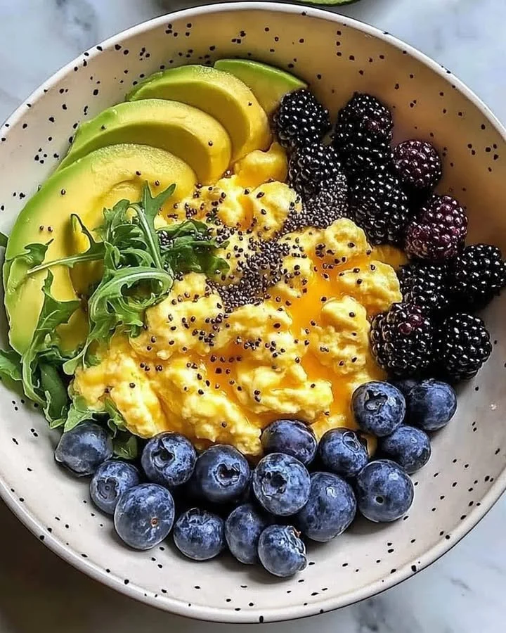 Colorful breakfast bowl with scrambled eggs, avocado slices, and mixed berries.