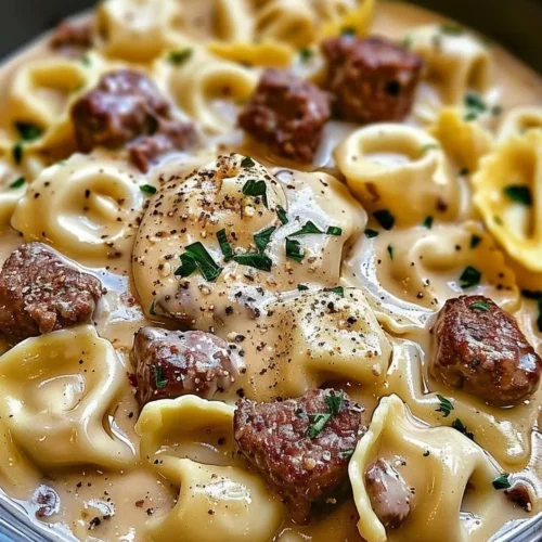 Cheesesteak tortellini served in rich provolone sauce, garnished with herbs.