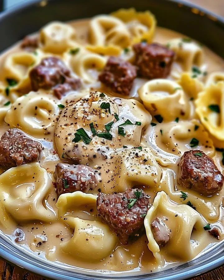 Cheesesteak tortellini served in rich provolone sauce, garnished with herbs.
