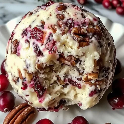 Cranberry pecan cheese ball garnished with nuts and herbs on a serving platter