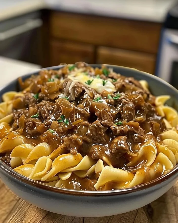 Delicious bowl of French onion beef and noodles topped with melted cheese