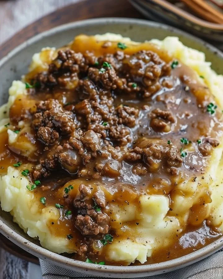 Ground beef and gravy served over creamy mashed potatoes in a warm bowl.