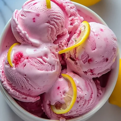 Delicious pink lemonade ice cream in a bowl with a slice of lemon on top.