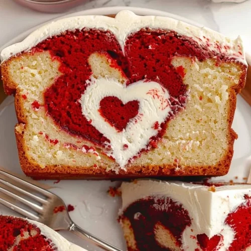 A slice of moist Red Velvet Loaf Cake with cream cheese frosting on a wooden table.