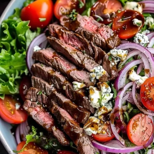 Sliced steak and gorgonzola salad topped with fresh greens and vinaigrette