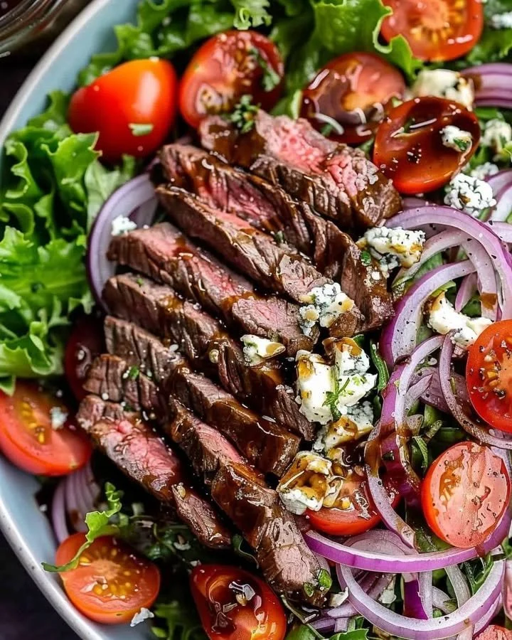 Sliced steak and gorgonzola salad topped with fresh greens and vinaigrette